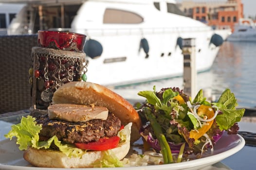 Gourmet beef burger with fois gras and gold leaf in a marina with a motor yacht in the background