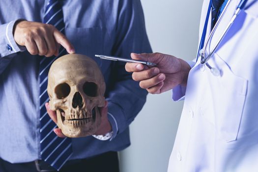 Doctor is holding a human skull in his hands and point to the skull for teaching and diagnose the symptom to the intern and medical students.