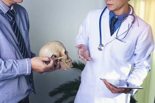 Doctor is holding a human skull in his hands and point to the skull for teaching and diagnose the symptom to the intern and medical students.