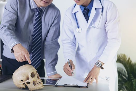 Doctor is holding a human skull in his hands and point to the skull for teaching and diagnose the symptom to the intern and medical students.