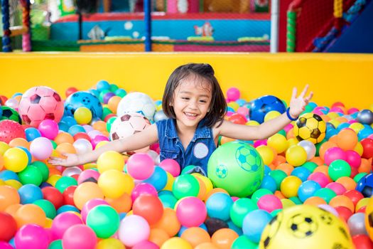 Happy little girl sitting in colourful balls. little girl with colored plastic balls. Funny child having fun indoors.