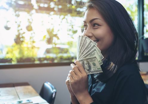 Portrait of a young surprised businesswomen with much money after signing the contract. Beautiful young businesswoman in black shirt holding money in hand and happy smile