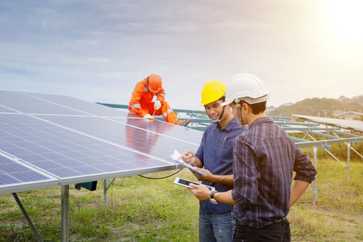 Engineers and workers in uniform and installs solid solar panels on a metal base in a solar farm.