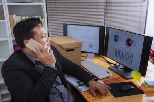 Businessman in suit talking on phone working on computer, busy entrepreneur making answering call sitting at office desk with computer, speaking to client by cell, using gadgets for business