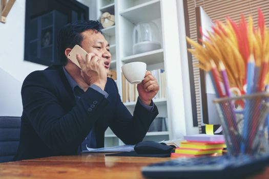 Businessman in suit talking on phone working on computer, busy entrepreneur making answering call sitting at office desk with computer, speaking to client by cell, using gadgets for business