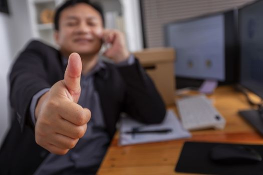 smiley successful businessman talking on the phone and showing thumbs up in office