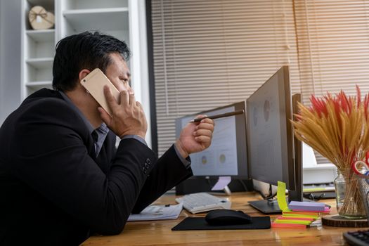 Businessman in suit talking on phone working on computer, busy entrepreneur making answering call sitting at office desk with computer, speaking to client by cell, using gadgets for business