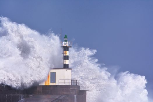 Stormy wave over lighthouse and pier of San Esteban de Pravia in Asturias, Spain.