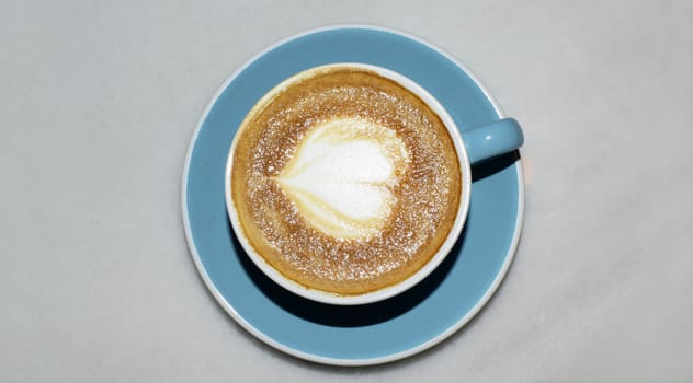 A cup of coffee with heart pattern in a blue cup on grey background.