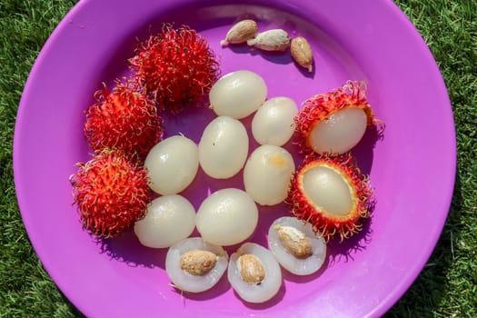 Close up of rambutan, whole and peeled fruits. Top view Healthy fruits on purple background. Ready to Eat Sweet Bali Fruit. Fruit is rounded oval single-seeded berry covered with fleshy pliable spines