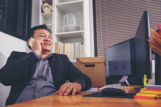 Businessman in suit talking on phone working on computer, busy entrepreneur making answering call sitting at office desk with computer, speaking to client by cell, using gadgets for business