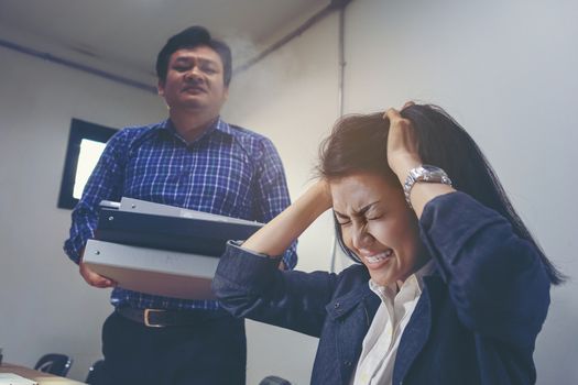 Deadline stress concept - furious business woman sitting at desk in office and shouting while holding hands on head with stress from hard work