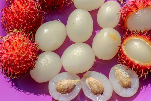 Close up of rambutan, whole and peeled fruits. Top view Healthy fruits on purple background. Ready to Eat Sweet Bali Fruit. Fruit is rounded oval single-seeded berry covered with fleshy pliable spines