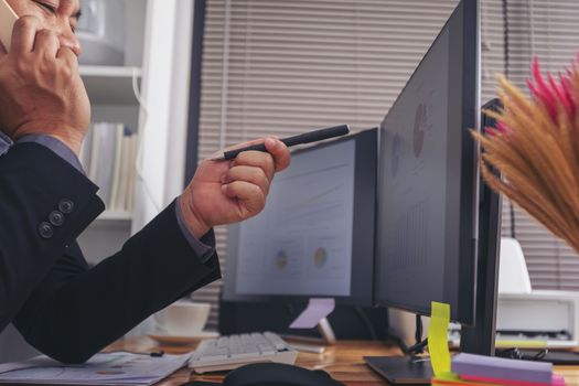 Businessman in suit talking on phone working on computer, busy entrepreneur making answering call sitting at office desk with computer, speaking to client by cell, using gadgets for business