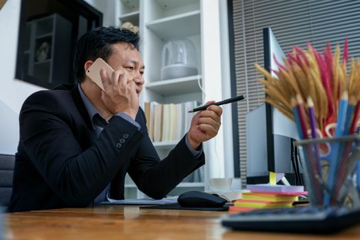 Businessman in suit talking on phone working on computer, busy entrepreneur making answering call sitting at office desk with computer, speaking to client by cell, using gadgets for business