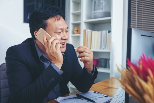 Businessman in suit talking on phone working on computer, busy entrepreneur making answering call sitting at office desk with computer, speaking to client by cell, using gadgets for business