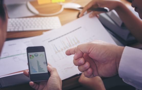 Businessman giving presentation on  mobile phone screen to colleagues in office. Business meeting time. Idea presentation, analyze plans.