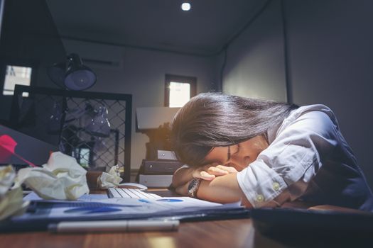 Deadline stress concept - furious business woman sitting at desk in office and shouting while holding hands on head with stress from hard work