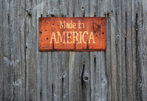 Rusty metal sign on wooden wall with the phrase: Made in America.