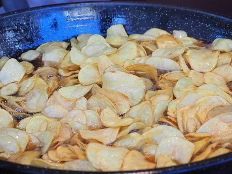 Frying chips in a black pan with a lot of boiling oil in a restaurant.