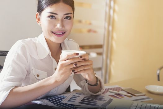 Happy casual beautiful woman working on a laptop and graph paper in the office desk