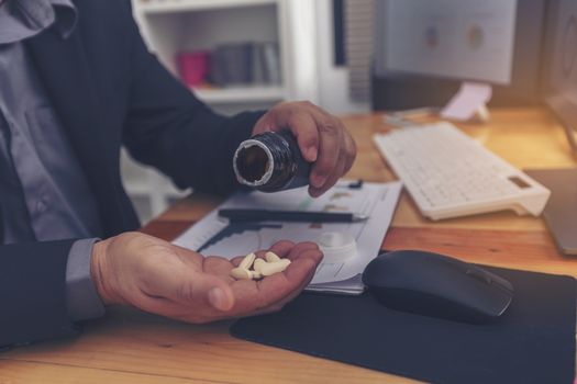 Stressed businessman having severe headache, holding painkiller remedy pill. Stress job