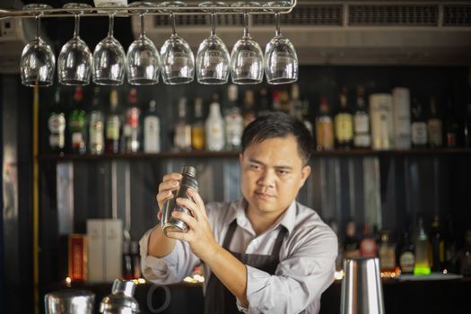 Bartender mixing a cocktail drink in cocktail shaker at bar counter