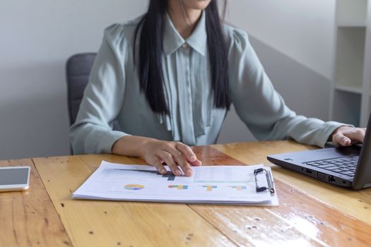 Beautiful young businesswoman doing some paperwork while sitting at office desk in front of computer.