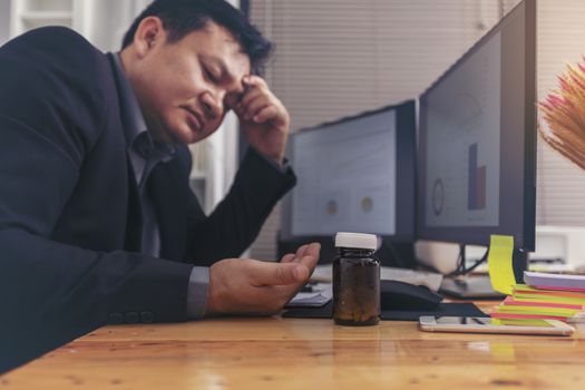 Stressed businessman having severe headache, holding painkiller remedy pill. Stress job