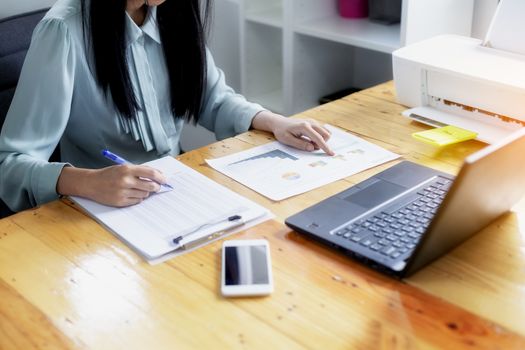 Beautiful young businesswoman doing some paperwork while sitting at office desk in front of computer.