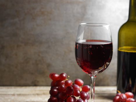 Glass of red wine on a wooden table in a rustic and vintage wine bar with grapes fruit and a bottle of wine on background closeup view.