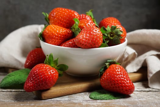 Strawberry concept with a group of ripe red strawberries in a white bowl close up frontal view on a vintage rustic wooden table on background.