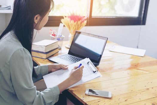 Beautiful young businesswoman doing some paperwork while sitting at office desk in front of computer.