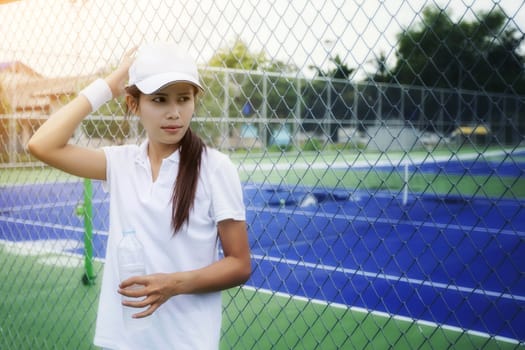 Beautiful young woman drinking water on the tennis court after playing tennis to exercise. Health Care Concept