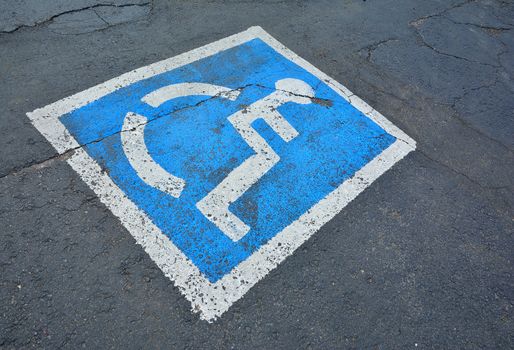 Disabled blue parking sign painted on dark asphalt.