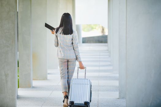 Portrait of business woman looking digital tablet with white travel bag on walkway while waiting to travel to the destination 