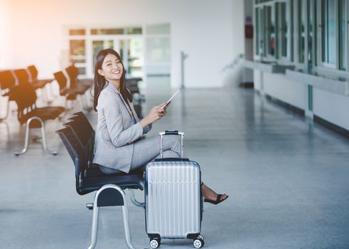 Portrait of business woman looking digital tablet with white travel bag While waiting to travel to the destination 
