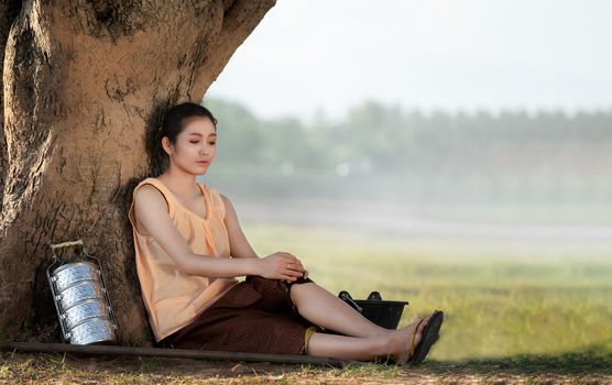 A beautiful Thai woman sat to relax under the tree, tired from working in rural areas.