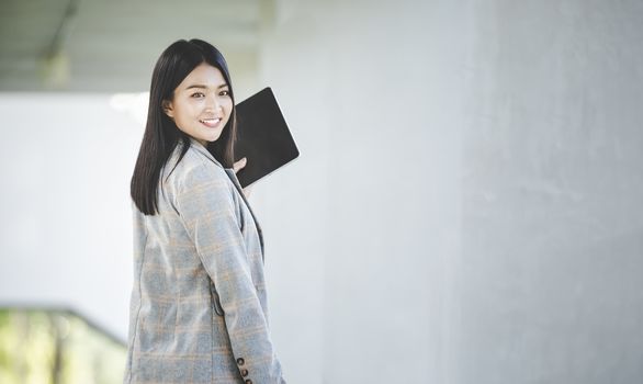 Portrait of business woman looking digital tablet with white travel bag on walkway while waiting to travel to the destination 