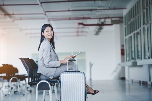 Portrait of business woman looking digital tablet with white travel bag While waiting to travel to the destination 