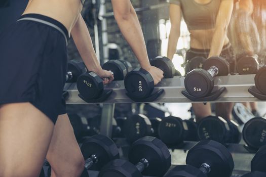 Close up of a beautiful woman reaching for a dumbbell to exercise in the gym