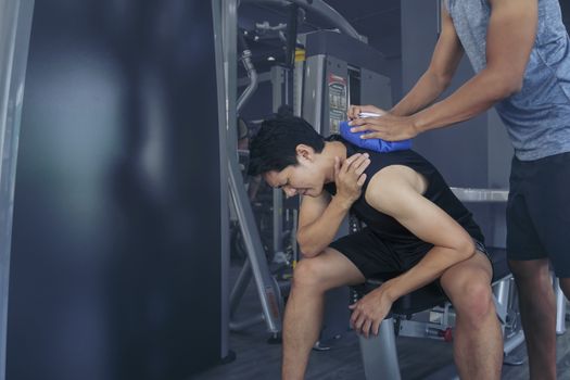 Handsome young man who is feeling pain from exercise and received an ice pack from his friend to relieve the pain