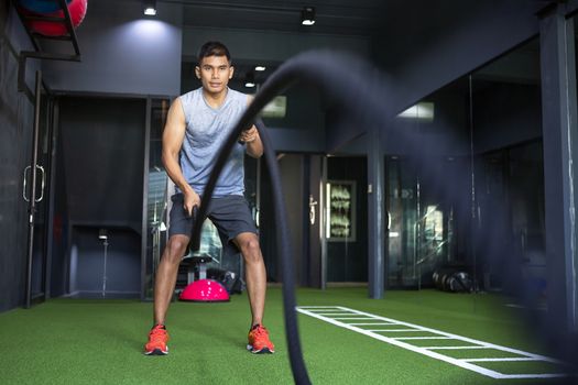 Man wearing a tank top to exercise at the gym with battle ropes during his fitness workout. High-Intensity Interval Training.