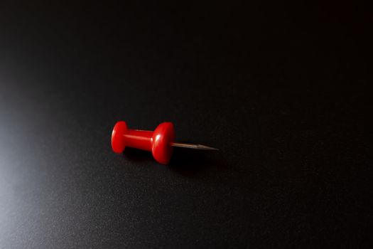 A closeup shot of a single plastic handled red pushpin on a black surface