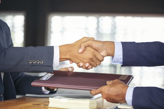 Young business people shaking hands in the office. Finishing successful meeting. Businessman holding pens and holding graph paper are meeting to plan sales to meet targets set in next year.