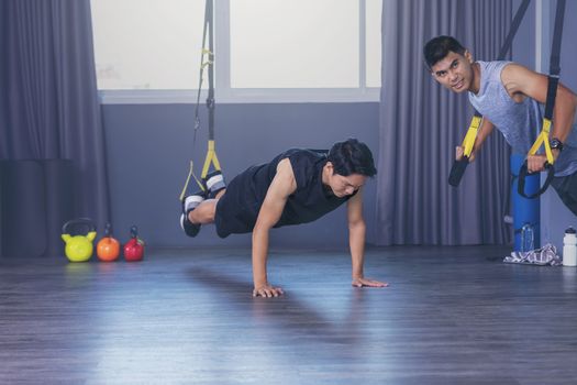 Group of sports people are training indoors with TRX. Two attractive young man and handsome man are working out in gym