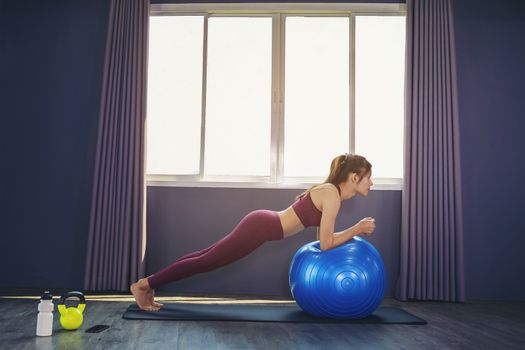 Beautiful woman is exercising by playing Pilates ball happily in a public gym.