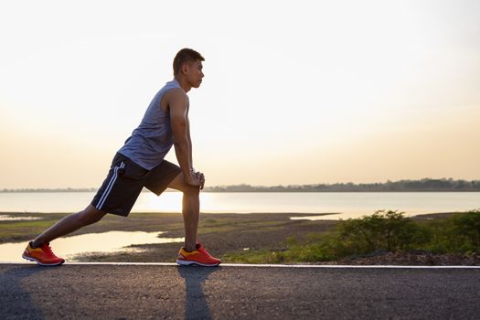 Shot of flexible young man warms up before jogging on the road in the park. People, sport, fitness and flexibility concept