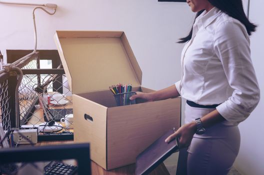 Upset female employee packing belongings in box, frustrated stressed girl getting fired from job ready to leave on last day at work. sad office worker desperate from work
