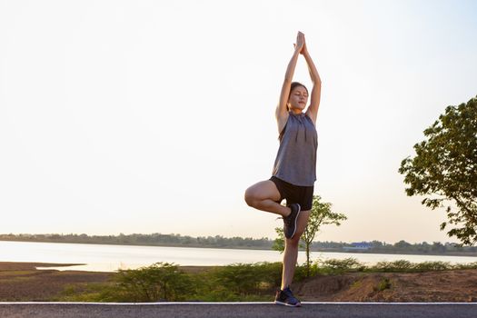 Shot of flexible young woman warms up before jogging on the road in the park. People, sport, fitness and flexibility concept